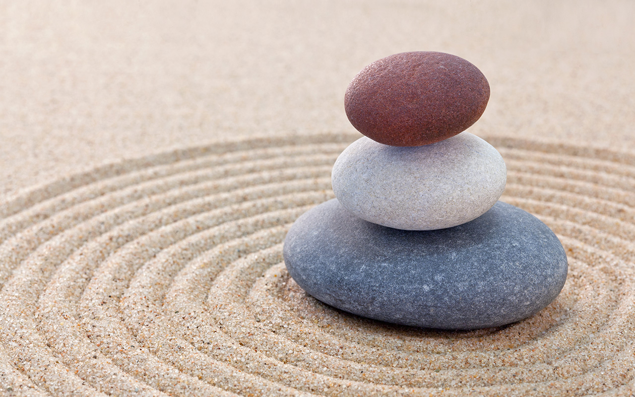 Three pebbles stacked on a circular raked zen garden